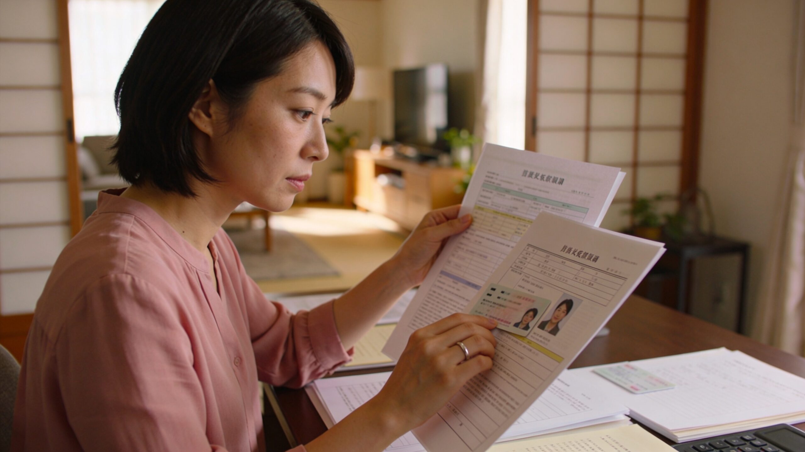 机の上で婚約者の身辺書類を慎重に確認する30代女性。指に小さな指輪をはめ、穏やかで思慮深い表情。