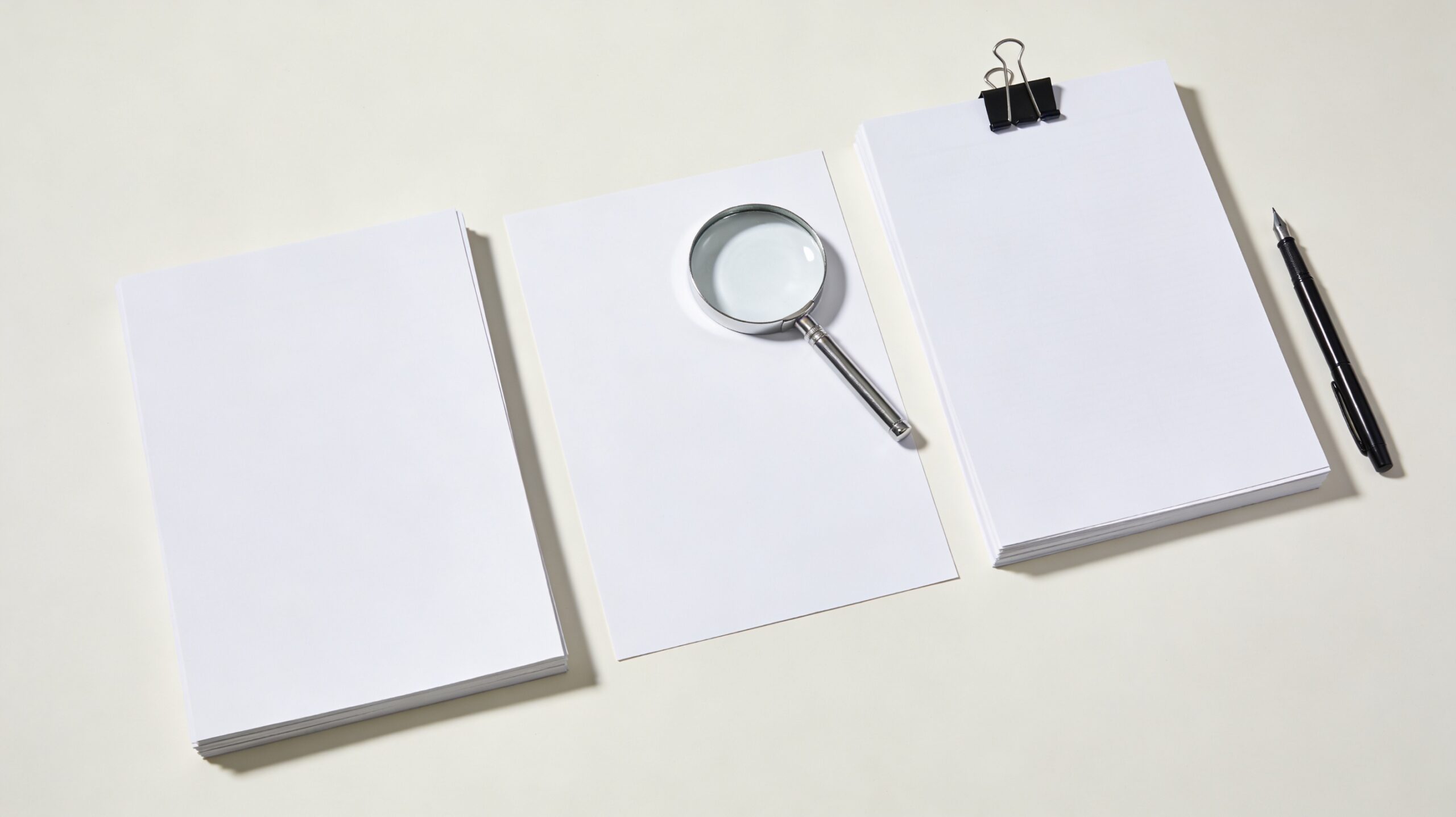 複数の白い書類束とシルバー虫眼鏡と万年筆のミニマル現代写真。戸籍調査と相続人探索を象徴。
