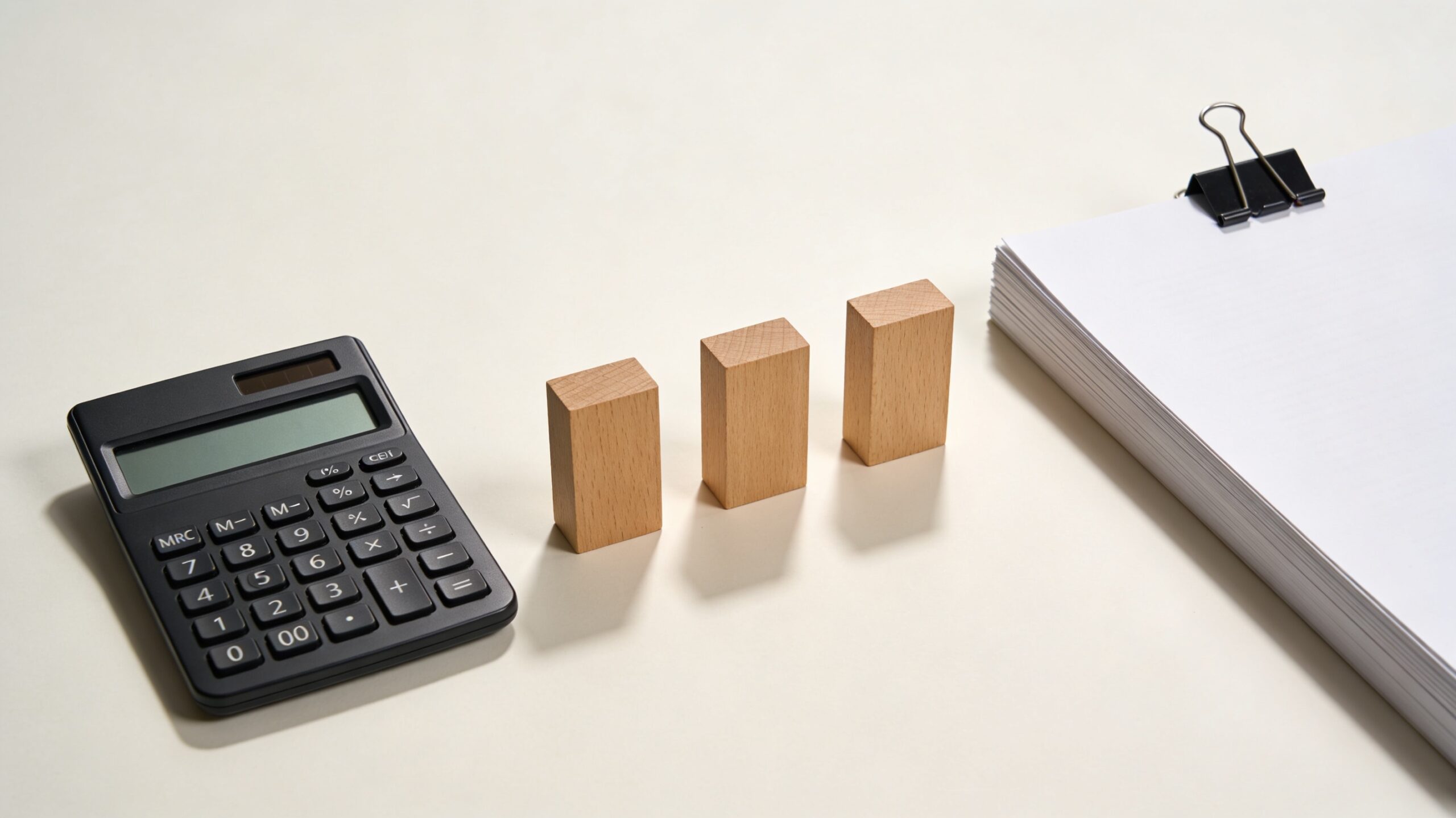 計算機・横並びの3本の木ブロック・書類束のミニマル現代写真。3つの料金プラン(時間制・成功報酬・パック)を比較する場面を象徴。